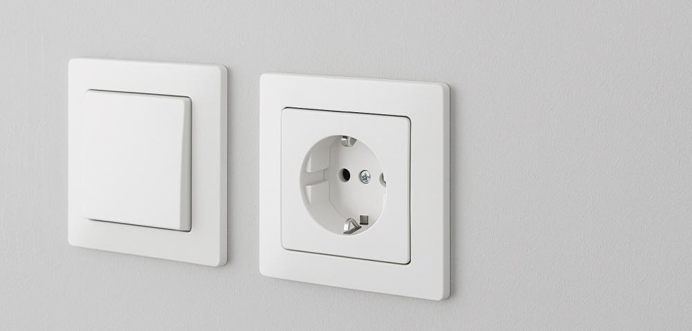Schaltermaterial mit Lichtschalter und Steckdose auf grauer Wand – Elektroinstallation von Elektro Pepi
